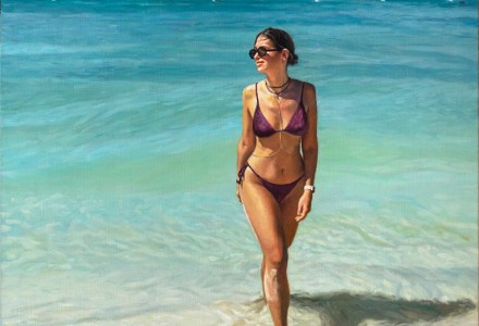 Mujer joven con bikini, gafas de sol y cadenas paseando por la orilla del mar con un barco al fondo.